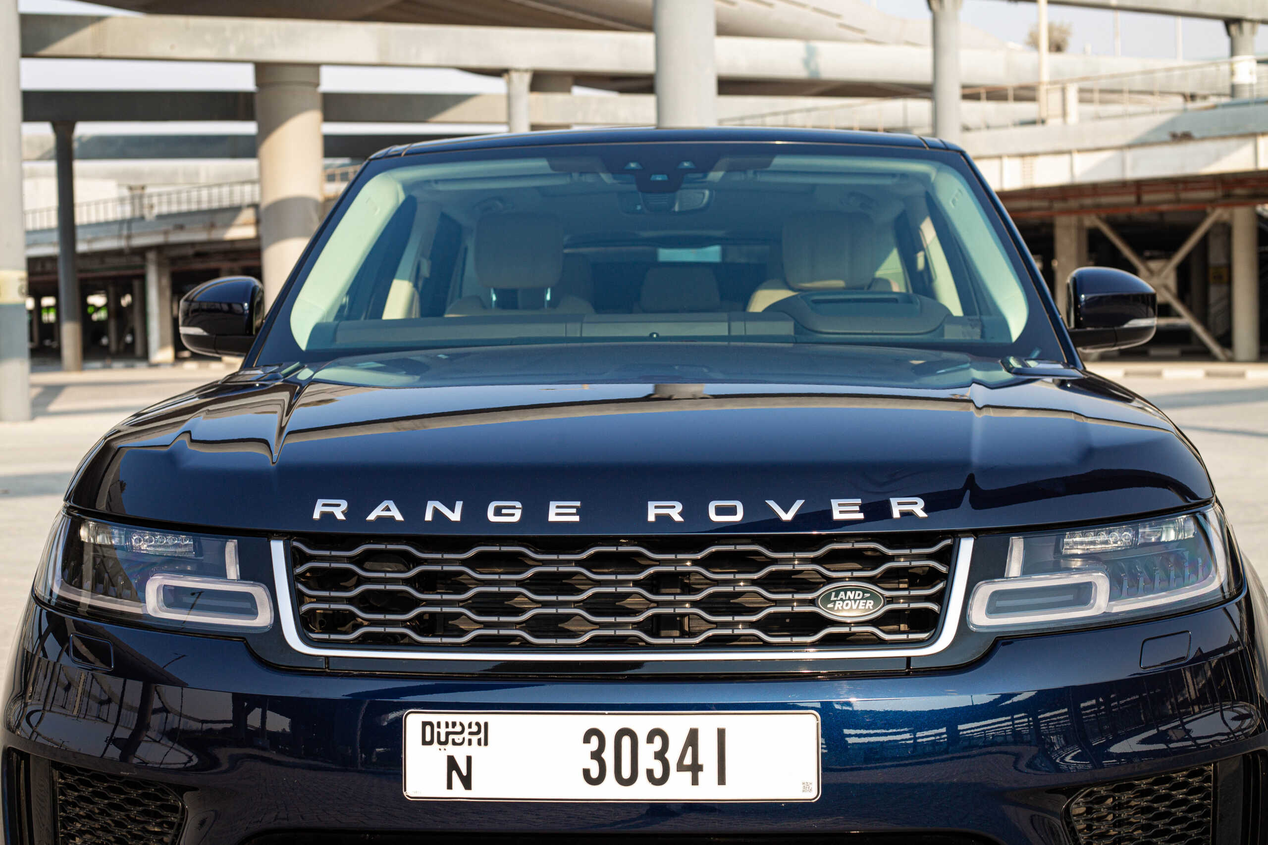 Front view of a navy blue Range Rover with its logo visible, parked in an urban setting under a modern overpass.